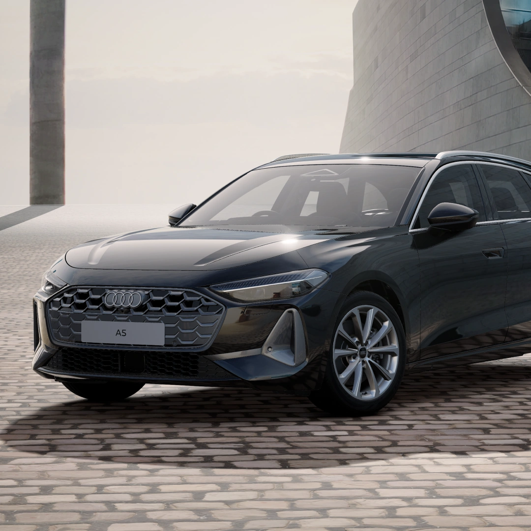 Front three-quarter view of a black Audi A5 Avant parked in a contemporary architectural setting, showcasing the Audi Singleframe grille, LED headlights, alloy wheels and sporty estate design.